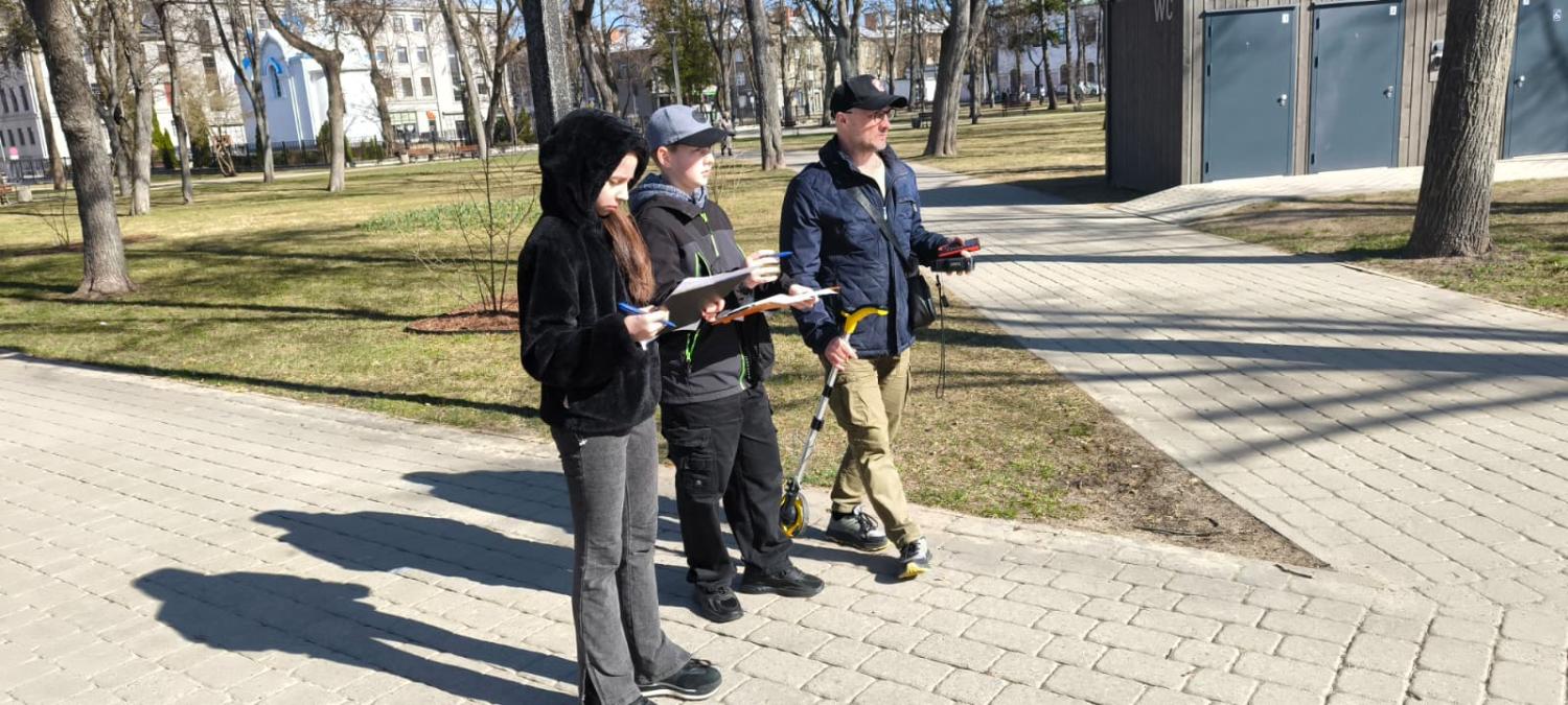 Skolēni un ģeodēzists ar instrumentu uz trotuāra